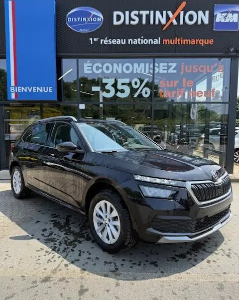 Vue 3/4 avant gauche d'un Skoda Kamiq noir 2024 garé devant une concession Distinxion avec reflets sur la carrosserie.