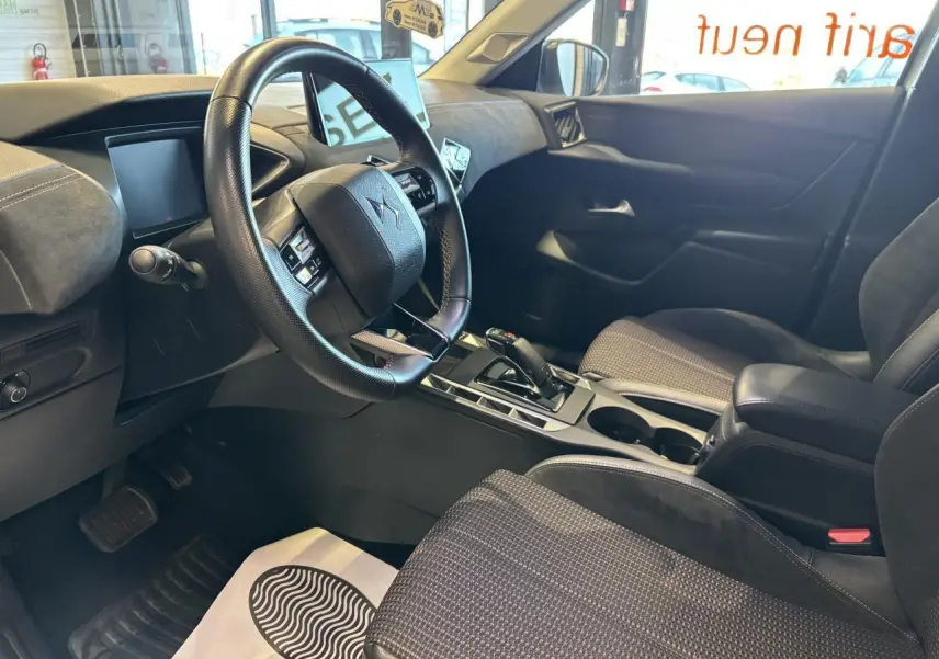 Vue intérieure côté conducteur du DS3 Crossback 2024 en Crystal Pearl, montrant le volant, la console centrale et les sièges noirs.