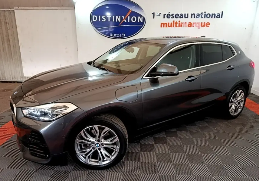BMW X2 hybride rechargeable gris foncé vue 3/4 avant droit, jantes alliage et prises de recharge visibles