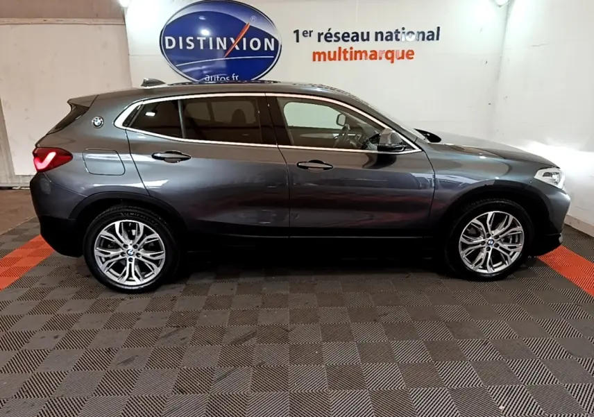 Vue de profil côté gauche d’un BMW X2 xDrive25e hybride rechargeable gris foncé avec jantes alliage et toit noir.