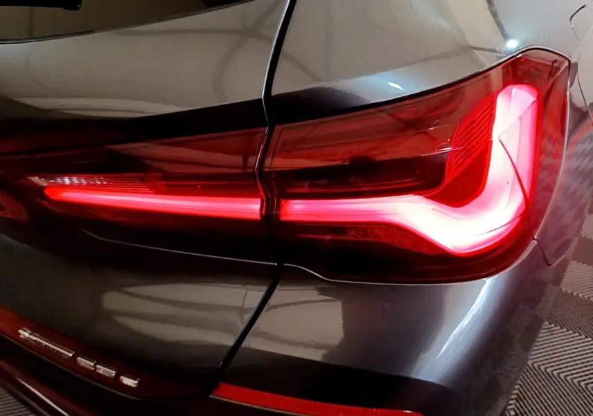 Gros plan sur le feu arrière droit rouge allumé du BMW X2 xDrive25e gris foncé, avec logo visible sur la malle arrière.