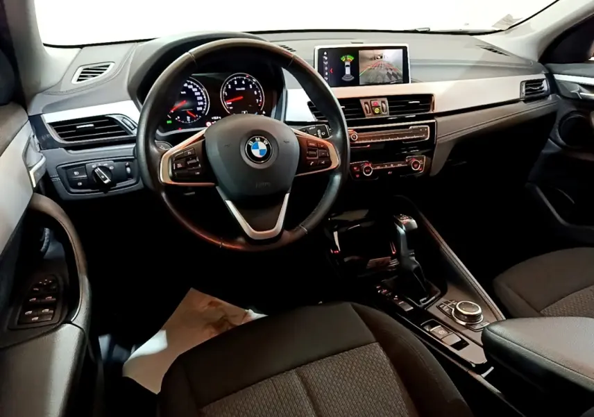 Vue intérieure avant du tableau de bord et volant cuir noir de la BMW X2 xDrive25e avec écran tactile et commandes multifonctions.