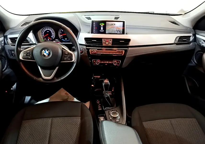Vue intérieure avant du tableau de bord et volant noir de la BMW X2 xDrive25e avec écran tactile central allumé.