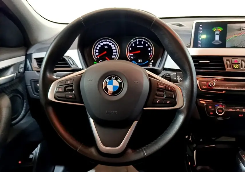 Vue intérieure centrée sur le volant cuir noir de la BMW X2 avec tableau de bord et écran tactile en arrière-plan.
