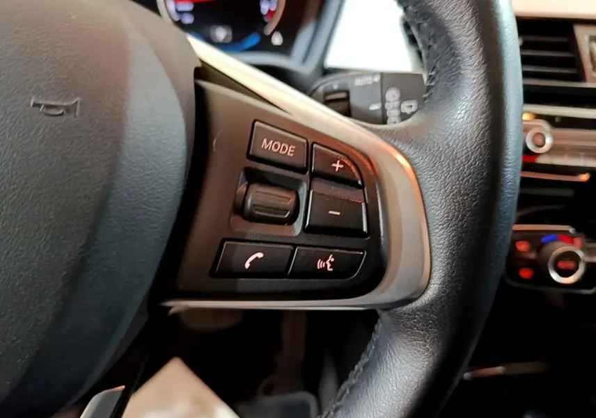 Gros plan sur le côté gauche du volant cuir noir de la BMW X2 xDrive25e avec commandes multimédia intégrées.