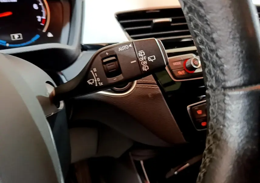 Gros plan sur la manette d’essuie-glace à gauche du volant cuir noir dans l’habitacle sombre d’une BMW X2 hybride rechargeable.