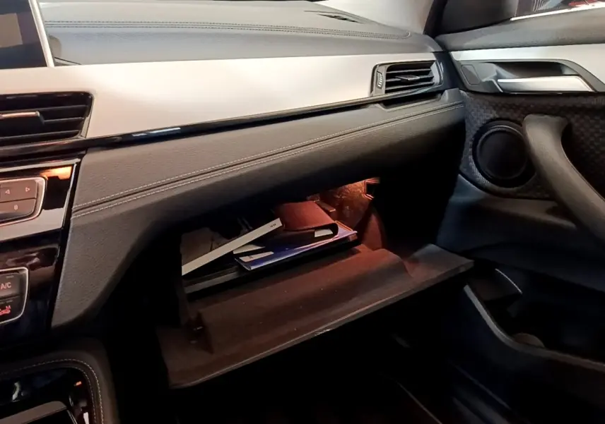 Vue intérieure côté passager du BMW X2 xDrive25e 2020 avec boîte à gants ouverte et éclairage intérieur orange.