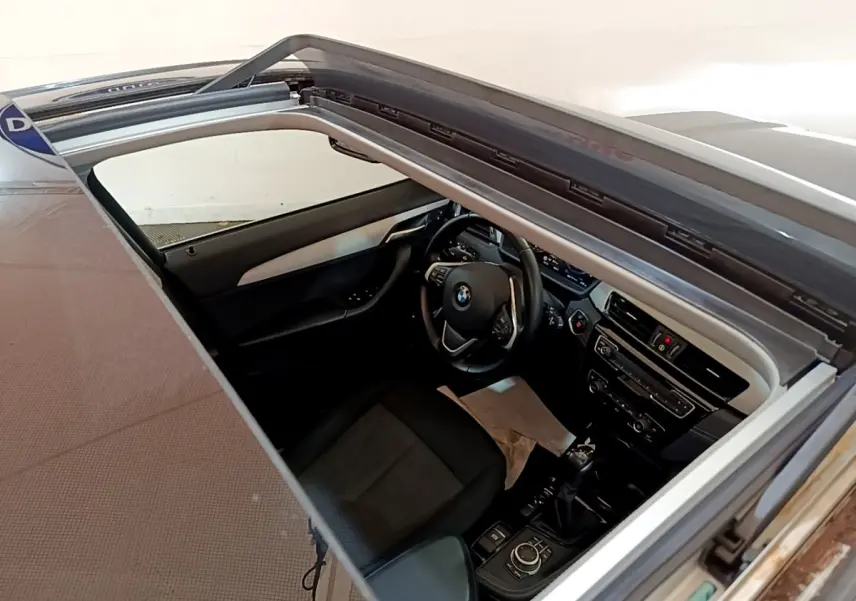 Vue intérieure plongeante du poste de conduite BMW X2 xDrive25e avec toit ouvrant et volant cuir multifonctions.