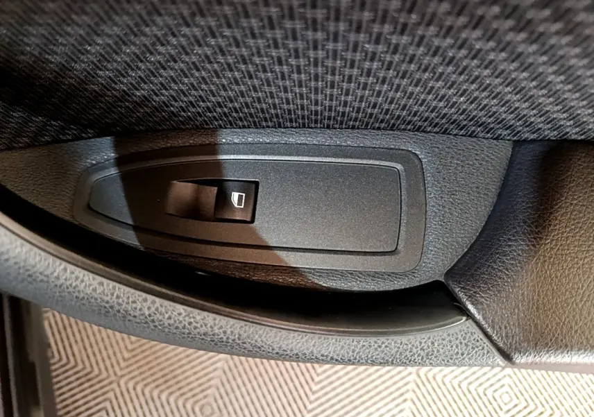 Gros plan sur le bouton de commande de lève-vitre intérieur en plastique noir, sur la porte côté conducteur d’un BMW X2 hybride.