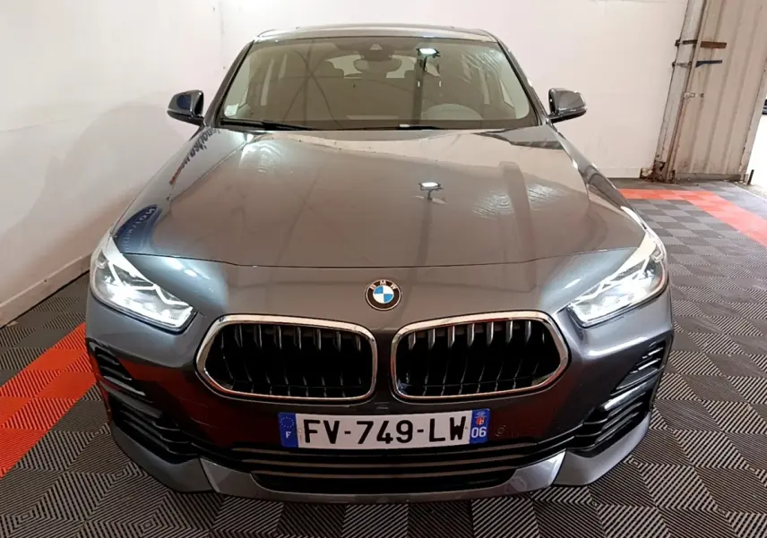 BMW X2 xDrive25e hybride rechargeable vue de face, couleur gris métallisé avec phares LED allumés dans un garage.
