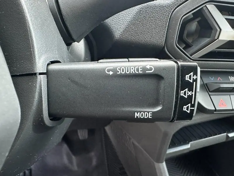 Gros plan sur la commande multimédia au volant du Dacia Duster 2025, intérieur noir avec détails fonction source et mode.