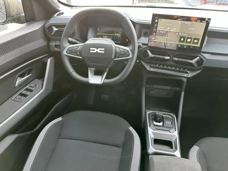 Vue intérieure centrée sur le poste de conduite du Dacia Duster 2025, avec volant multifonction et écran tactile.