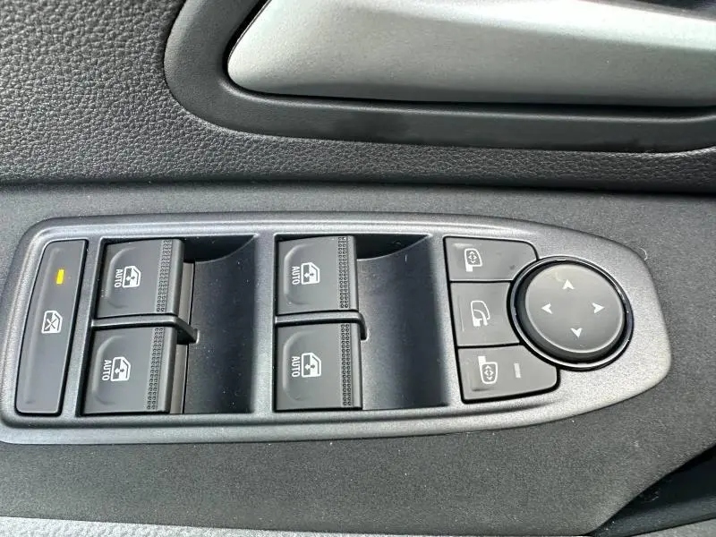 Gros plan sur les commandes des vitres électriques et rétroviseurs du côté conducteur d'un Dacia Duster 2025 Noir Nacré métallisé.