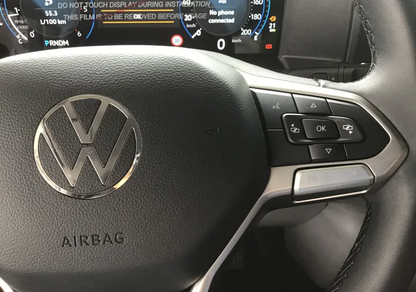 Gros plan sur le volant multifonction du Volkswagen Transporter T7, avec commandes intégrées et tableau de bord numérique visible.