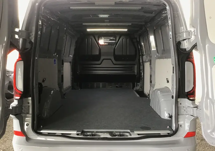 Vue arrière ouverte du Volkswagen Transporter T7 gris stone montrant l'espace de chargement vide et l'aménagement intérieur utilitaire.