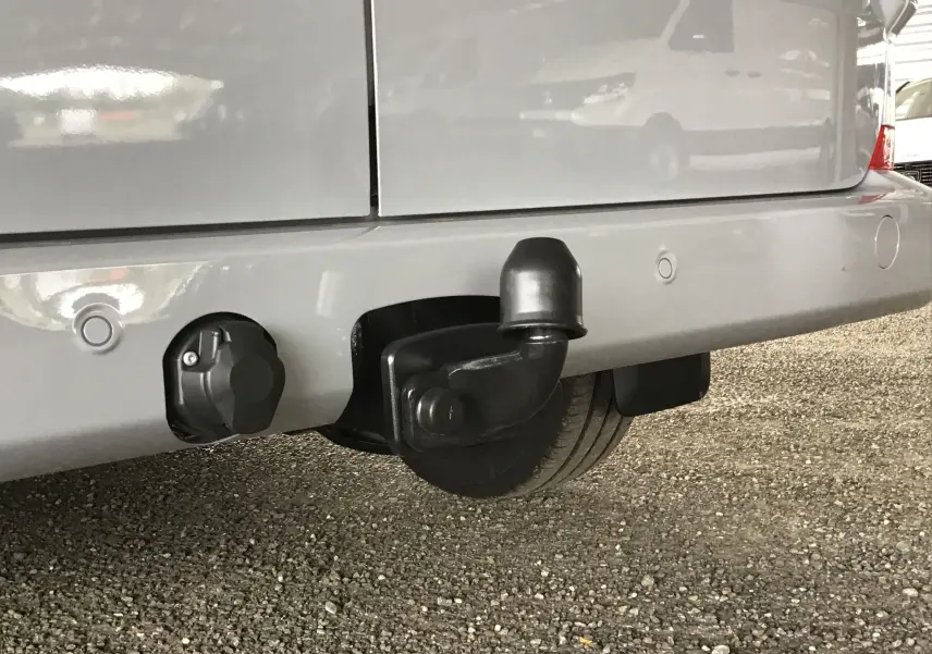 Gros plan sur l'attelage d'un Volkswagen Transporter T7 gris stone, vue arrière basse avec prise électrique visible.