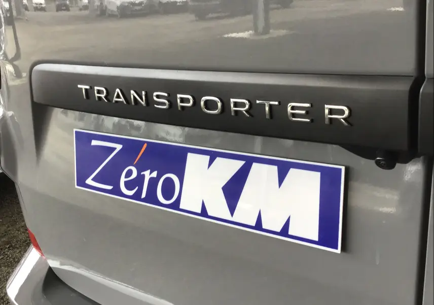 Gros plan sur l'arrière gris stone du Volkswagen Transporter T7 avec logo et plaque Zéro KM visible.
