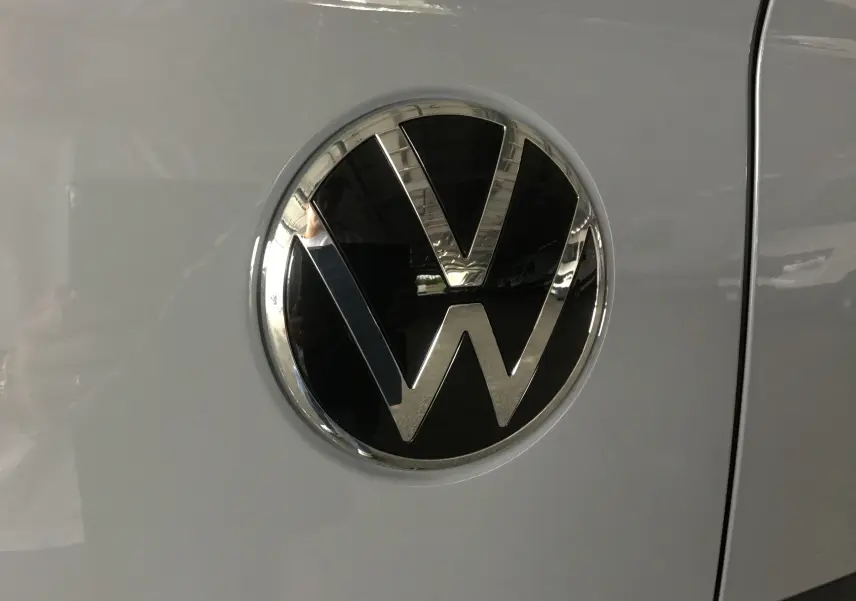 Gros plan sur l'emblème Volkswagen noir et chrome sur la porte latérale gris stone du Transporter T7 2025.