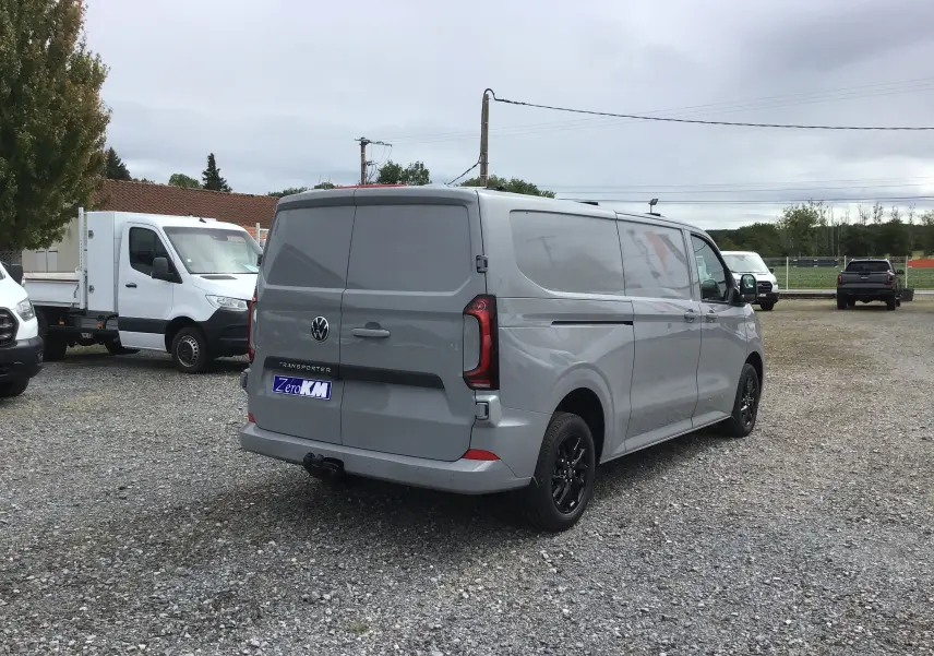 Volkswagen Transporter gris Stone vu en 3/4 arrière droit, avec barres de toit repliables et jantes noires.