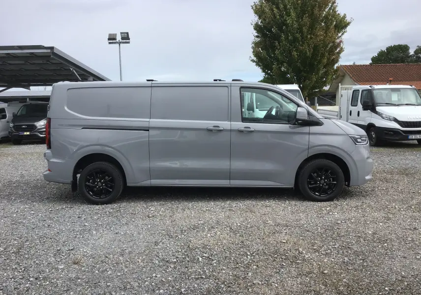 Vue de profil côté gauche d'un Volkswagen Transporter T7 gris stone avec jantes noires et barres de toit repliables.