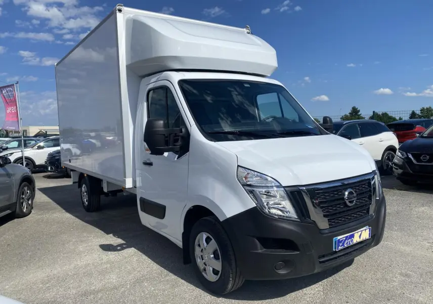Vue 3/4 avant droite d’un utilitaire Nissan Interstar blanc avec capucine, stationné en extérieur sous ciel bleu.