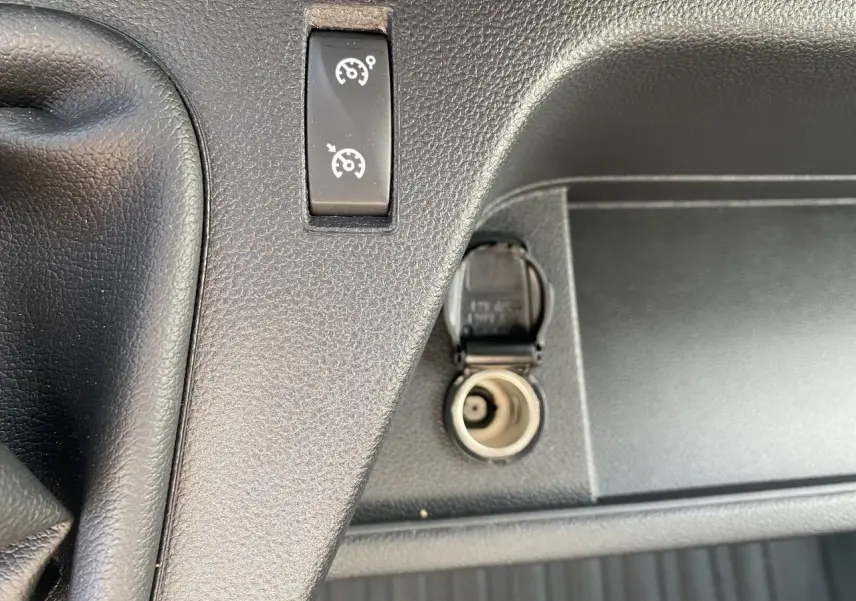 Prise 12 volts ouverte et bouton de régulateur de vitesse sur la console noire du Nissan Interstar blanc 2022.