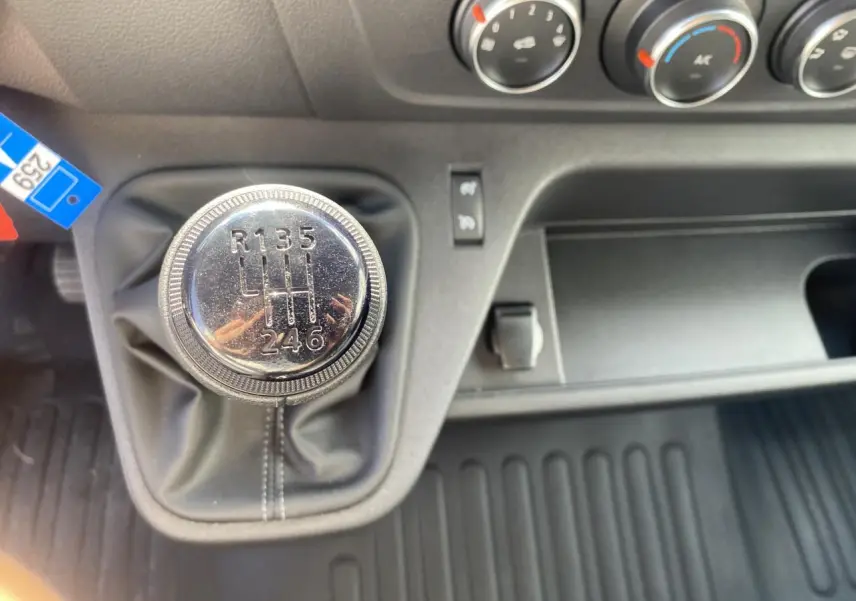 Gros plan sur le levier de vitesse manuel chromé du Nissan Interstar blanc avec commandes de climatisation en arrière-plan.