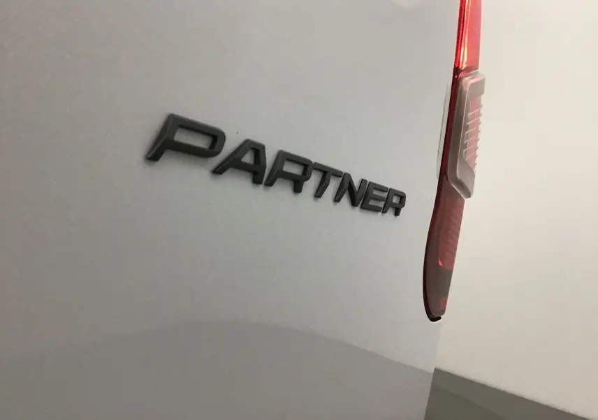 Gros plan sur l'arrière droit blanc d'un Peugeot Partner, mettant en valeur le logo noir "PARTNER" et le feu arrière rouge.