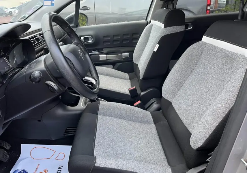Vue intérieure côté conducteur de la Citroën C3 2019, sièges gris clair et noir avec volant noir visible.