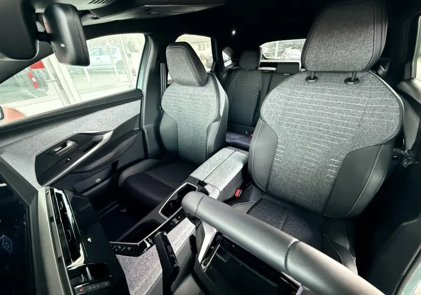 Vue intérieure avant du Peugeot 3008 Hybrid 2025, sièges tissu gris avec surpiqûres et accoudoir central assorti.