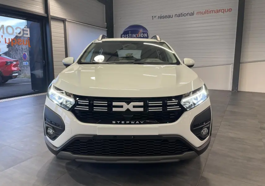 Vue avant d'une Dacia Sandero Stepway blanche Glacier avec calandre noire et signature lumineuse LED en showroom.