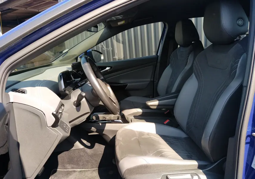 Vue intérieure côté conducteur du Volkswagen ID.4 bleu métal 2022, sièges en cuir et alcantara noirs avec tableau de bord moderne.