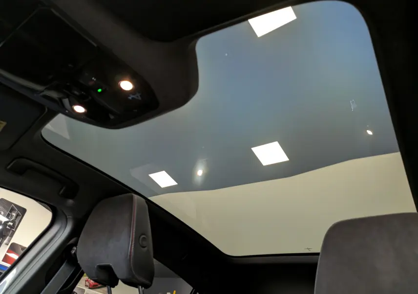 Vue intérieure du toit panoramique en verre du Renault Rafale gris schiste, mettant en valeur l'éclairage et les sièges avant.