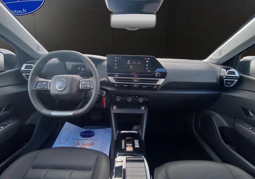 Intérieur de la Citroën C4 2025 vue de face, tableau de bord noir avec écran tactile central et volant multifonctions.