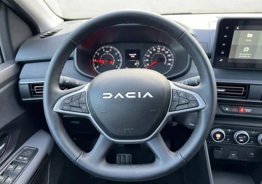 Vue centrée sur le volant noir du Dacia Sandero Stepway 2024, avec tableau de bord et écran tactile visibles.