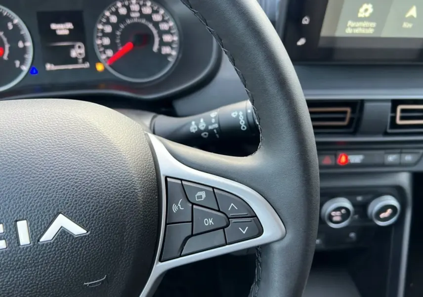 Gros plan sur le volant noir de la Dacia Sandero Stepway 2024, avec commandes multifonctions et tableau de bord en arrière-plan.