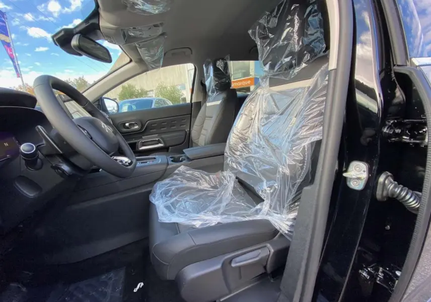 Intérieur avant droit du Citroën C5 Aircross noir Perla, sièges en cuir protégés par film plastique, tableau de bord visible.