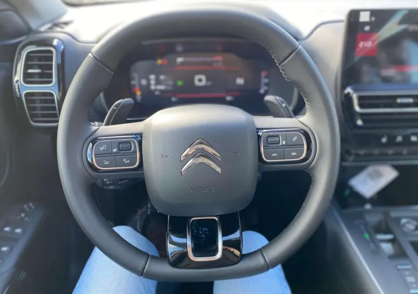 Vue centrée sur le volant noir du Citroën C5 Aircross 2025 avec commandes intégrées et tableau de bord numérique flou.