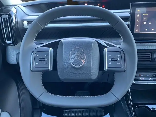 Vue rapprochée du volant gris foncé du Citroën C3 Aircross Hybrid 145 avec commandes intégrées et tableau de bord numérique.