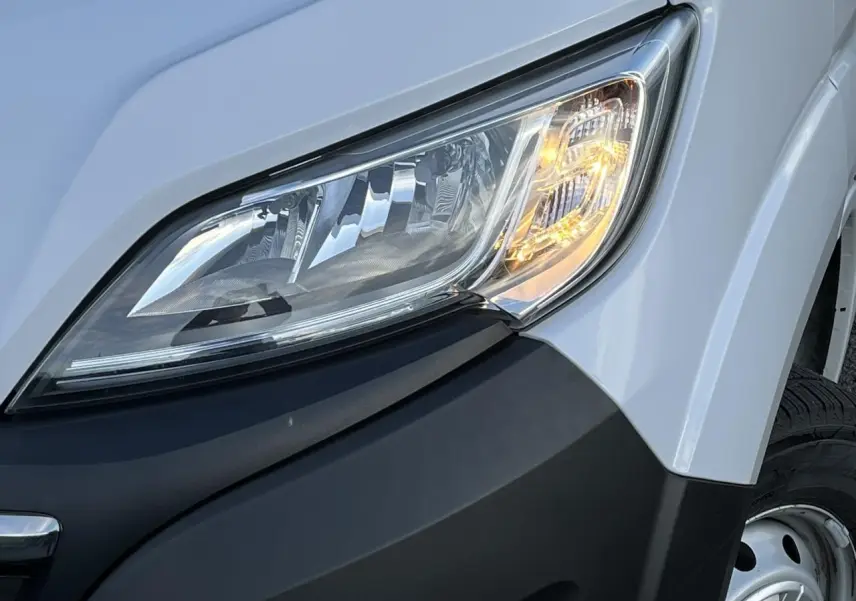 Gros plan sur le phare avant droit du fourgon blanc Opel Movano 2024 avec pare-chocs noir et jante acier visible.