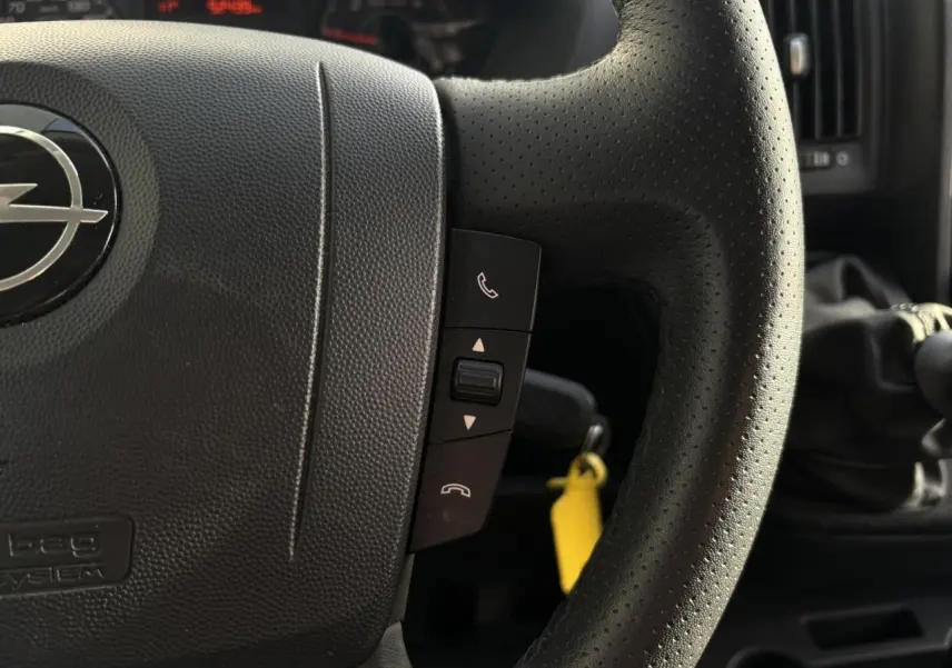 Gros plan sur le volant noir perforé de l’Opel Movano Fourgon 2024 avec commandes d’appel et levier de vitesses manuel visible.