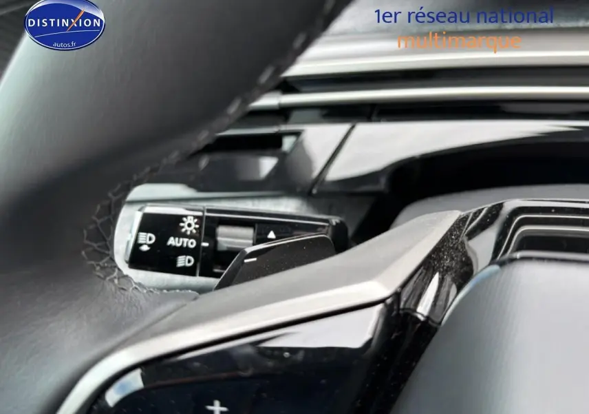 Gros plan sur le volant cuir noir et la commande des phares automatiques du Peugeot 5008 Hybrid 145 allure e-dcs6.