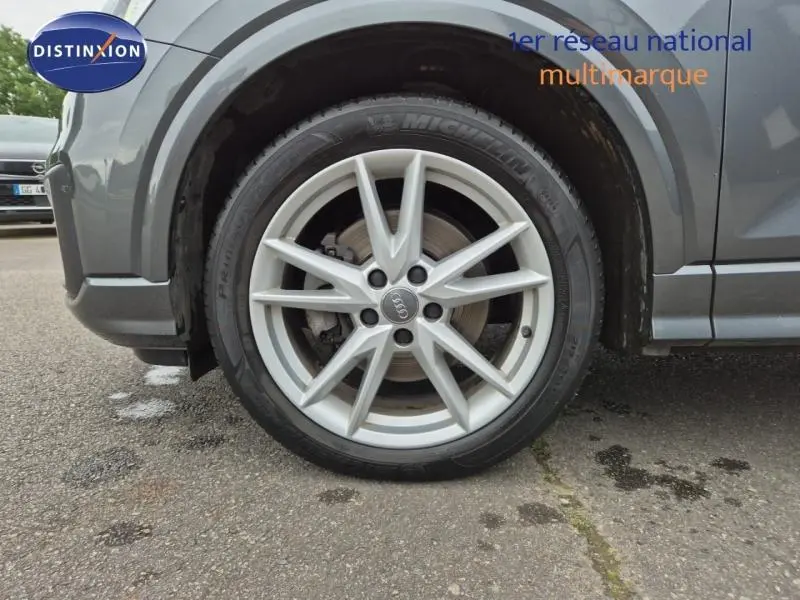 Gros plan sur la roue avant droite avec jante alu argentée d’un Audi Q2 gris Manhattan.
