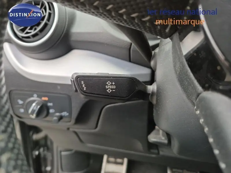 Gros plan sur la commande de régulateur de vitesse à gauche du volant dans l'Audi Q2 gris Manhattan de 2017.