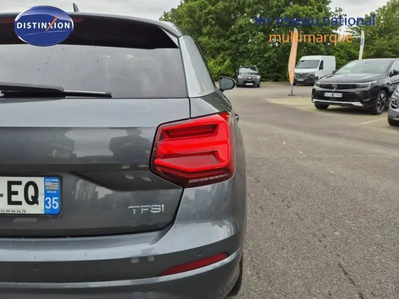 Vue arrière droite d'un Audi Q2 gris Manhattan avec feux arrière LED et badge TFSI visible.