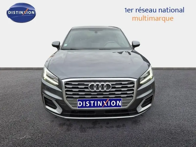 Vue avant d'un Audi Q2 gris Manhattan avec calandre hexagonale et feux LED allumés sur fond neutre.