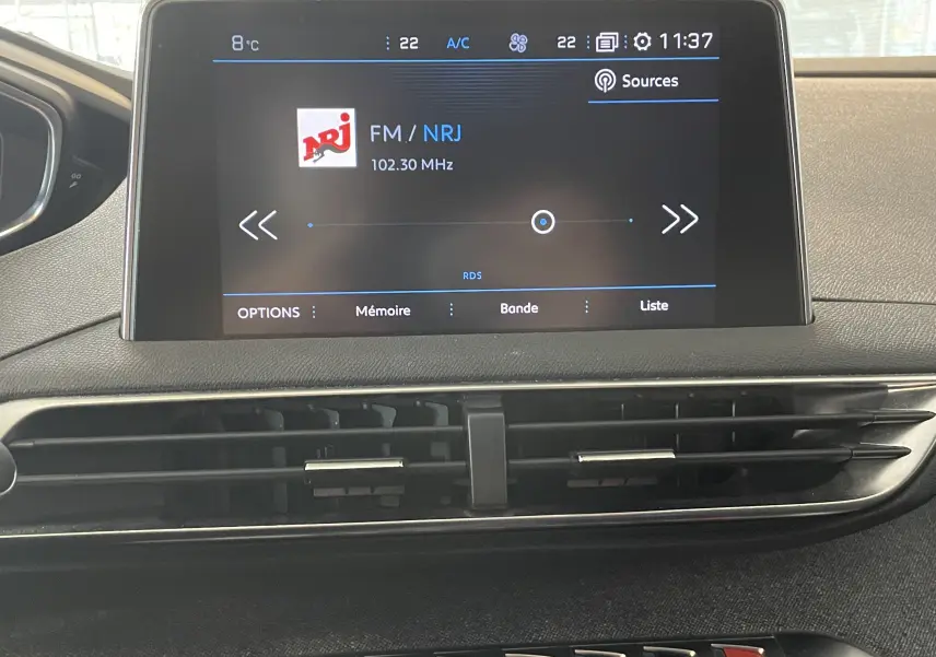 Écran central tactile du tableau de bord du Peugeot 5008 blanc nacré, affichant la radio FM NRJ à 102.30 MHz.