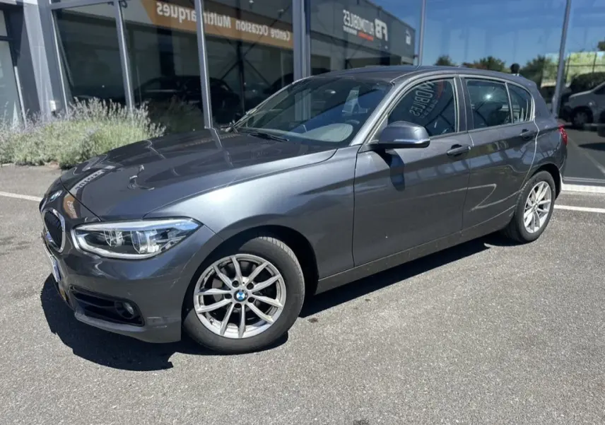 BMW Série 1 F20 gris foncé vue 3/4 avant droit, mettant en valeur ses jantes alliage et ses lignes épurées.
