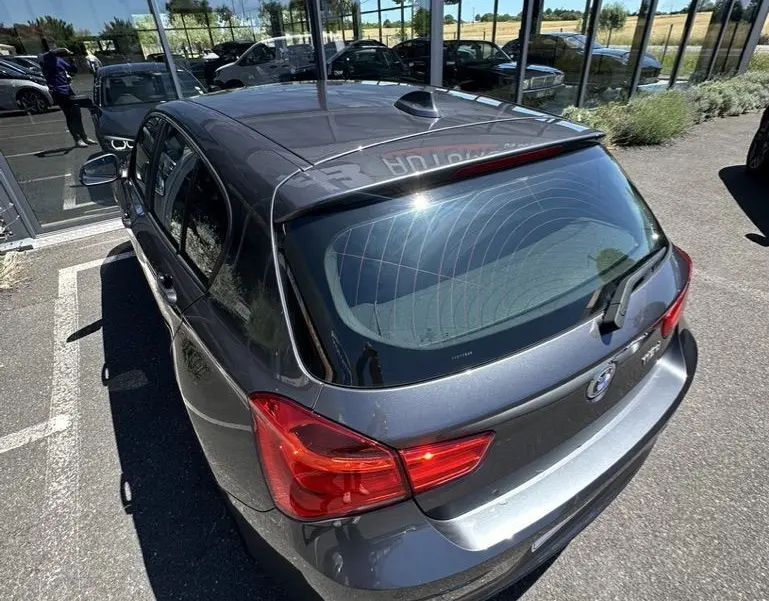 BMW Série 1 gris foncé vue en 3/4 arrière droit, soulignant les feux arrière et la lunette arrière teintée.