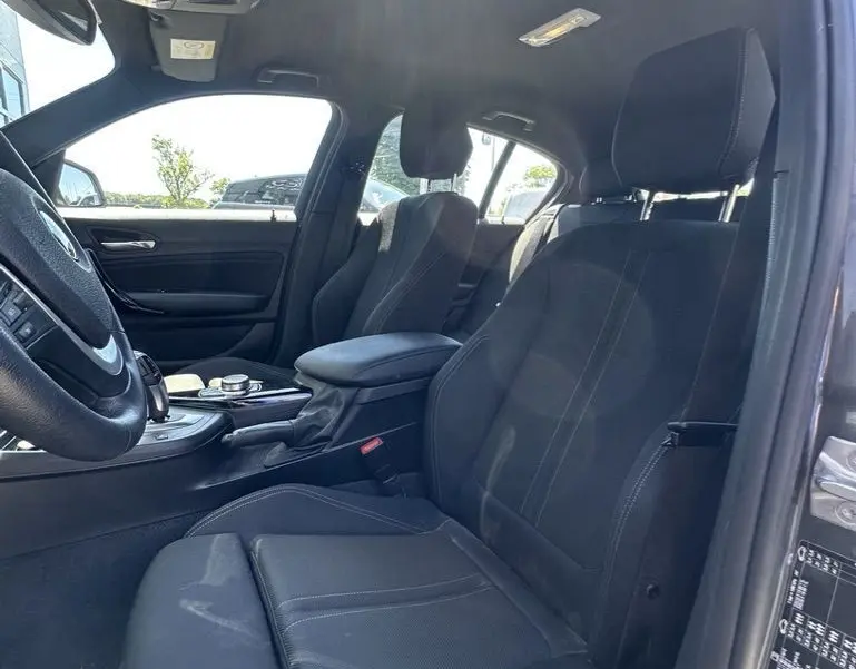 Intérieur avant côté conducteur d'une BMW Série 1 F20 gris foncé, sièges noirs avec surpiqûres blanches, console centrale visible.